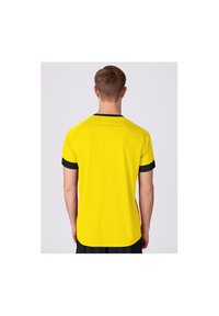 Gelbes Sportshirt mit kurzen schwarzen Ärmeln, rundem Halsausschnitt und glatter Textur, von hinten an einem Modell gezeigt.