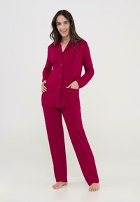 Conjunto de pijama rojo que incluye una camisa de botones con cuello y dos bolsillos frontales, combinado con pantalones rectos a juego. Tela suave y lisa.