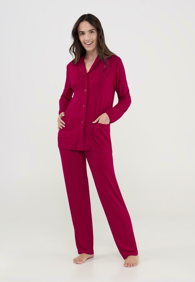 Conjunto de pijama rojo que incluye una camisa de botones con cuello y dos bolsillos frontales, combinado con pantalones rectos a juego. Tela suave y lisa.