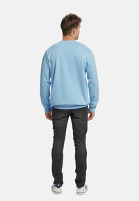 Lyseblå genser med lange ermer, rund hals og ribbestrikkede mansjetter, kombinert med mørkegrå jeans og hvite joggesko.