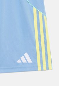 Maglietta sportiva azzurro chiaro con dettagli gialli e bianchi, caratterizzata da tre strisce verticali e un logo bianco in basso a sinistra.