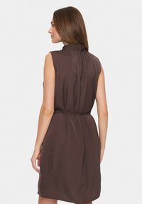 Rochie marron fără mâneci, cu guler înalt, spate pliat și buzunare laterale. Textură fină, cu talie ajustată și tiv evazat.