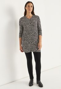 Blumen-Tunika mit langen Ärmeln in Schwarz, mit einem weißen Muster, kombiniert mit schwarzen Leggings und Stiefeletten. Glatte Textur, lässige Passform.