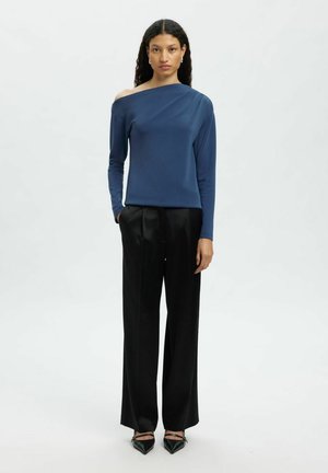 Tamsiai mėlynas, bepečių viršus, pagamintas iš lygaus audinio, derinamas su juodomis plačiomis kelnėmis. Apranga turi ilgomis rankovėmis ir minimaliais dizaino akcentais.