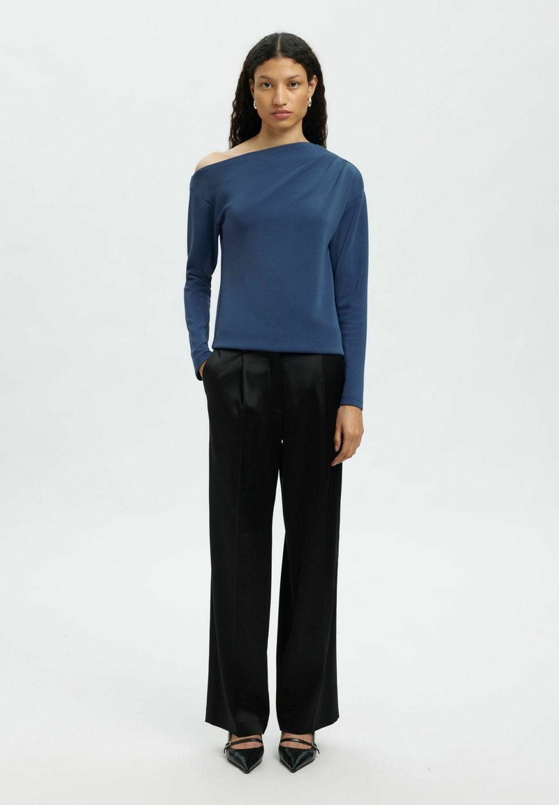 Navyblaues Off-Shoulder-Oberteil aus glattem Stoff, kombiniert mit schwarzen, weit geschnittenen Hosen. Das Outfit hat lange Ärmel und minimale Designmerkmale.