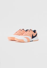 Sneakers med en hvit og ferskenfarget overdel, marineblå aksenter, teksturerte meshpaneler, flate lisser og en gummisåle med et sikksakkmønster.