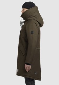 Parka verde măsliniu cu guler înalt, glugă ajustabilă și buzunare frontale. Prezintă o pată cu logo pe umăr și un accent triangular.