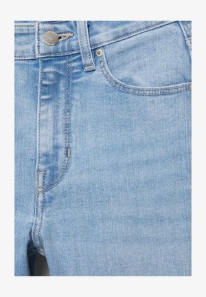 Jasnoniebieskie dżinsy z denimu na zbliżeniu, pokazujące przednią kieszeń, szlufkę na pasek, metalowy guzik oraz detale kontrastowych szwów.