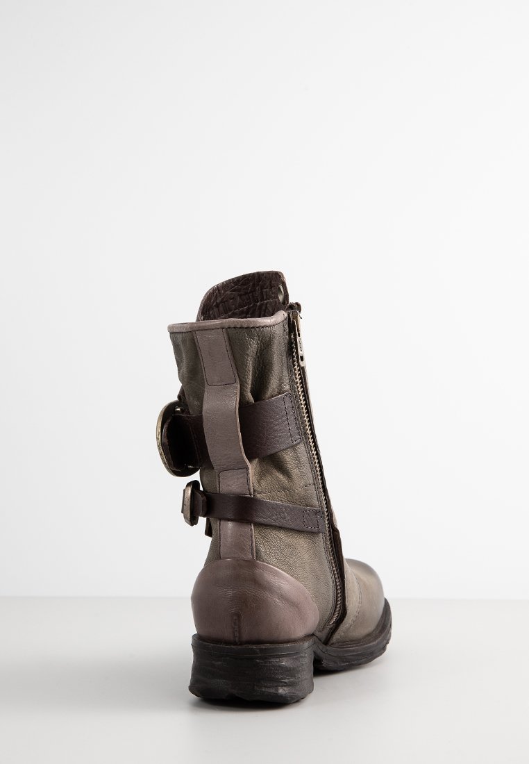 Bottine en cuir marron avec un bout arrondi, un dos texturé, fermeture éclair à l'arrière, et brides réglables à la cheville. Semelle en caoutchouc.