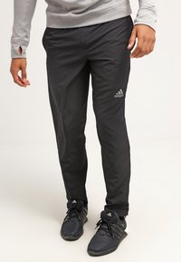 Černé sportovní kalhoty vyrobené z lehkého materiálu, s úzkým střihem a vyšitým logem Adidas na levém stehně.