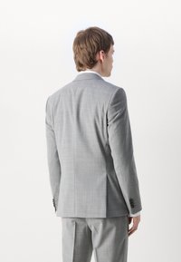 Giacca da abito grigia su misura con un motivo a quadri discreto. Presenta spalle strutturate, spacco singolo e polsini con bottoni. Vista da dietro.