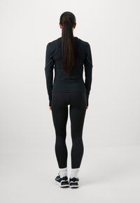 Zwarte long sleeve top met een aansluitend ontwerp, gecombineerd met zwarte leggings en sportschoenen. Gladde textuur, minimale details en geen patronen.