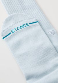 Calcetines cortos azul claro fabricados con tela texturizada. Entre sus características se incluyen un diseño acanalado, un logo en turquesa de "STANCE" y un detalle de logo blanco redondo.