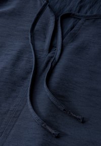 Donker marineblauwe stof met een gladde textuur, voorzien van een V-halslijn en verstelbare trekkoorden. Gedetailleerde stiksels langs de naden.