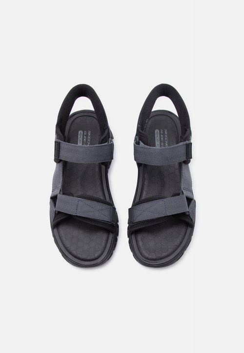 Paire de sandales noires et grises à bout ouvert avec des sangles ajustables et des semelles rembourrées texturées, vues de dessus sur un fond clair.