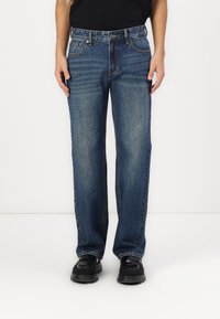 Rechtafstaande blauwe denim jeans met een medium wash, vijf-pocket ontwerp, contrasterende stiksels en een standaard tailleband. Soepele textuur.