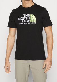 Černé bavlněné tričko s bílým a zeleným logem „THE NORTH FACE“ a nápisem „NEVER STOP EXPLORING“ na přední straně. Krátké rukávy, kulatý výstřih.