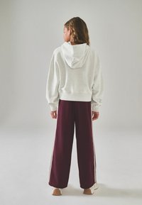 Felpa grigia con tasca a marsupio, caratterizzata da una finitura testurizzata e cappuccio. Pantaloni a gamba larga bordeaux con strisce bianche laterali e una vestibilità comoda.