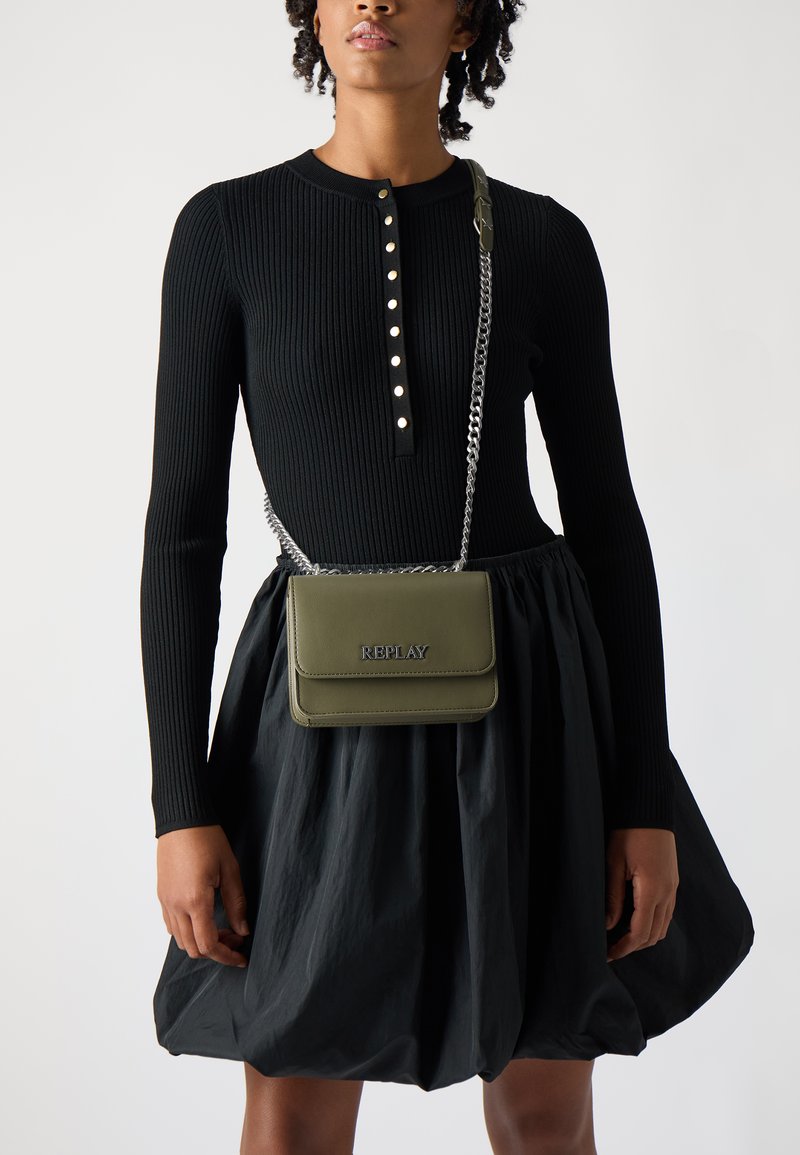 Grønn skinn crossbody bag med glossy finish, kjede-reim og preget "REPLAY"-logo. Modellen har på seg en ribbet svart topp og ett svart skjørt.