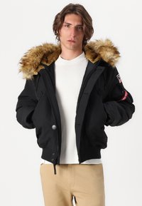 Black bomber jacket with a fur-lined hood. Features a front zip, side pockets, and a patch on the left arm. Smooth fabric texture.