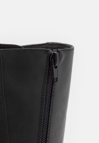 Botín de cuero negro hasta el tobillo con un cierre lateral, textura suave y costuras reforzadas a lo largo de las uniones. El corte superior es elegante y estructurado.