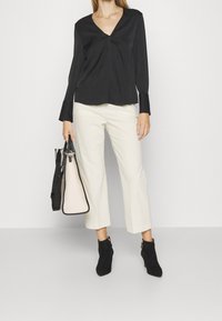 Blusa nera a maniche lunghe con scollatura a V e dettaglio a torsione, abbinata a pantaloni cropped a gamba larga color crema e stivali neri alla caviglia. Porta una borsa bicolor.