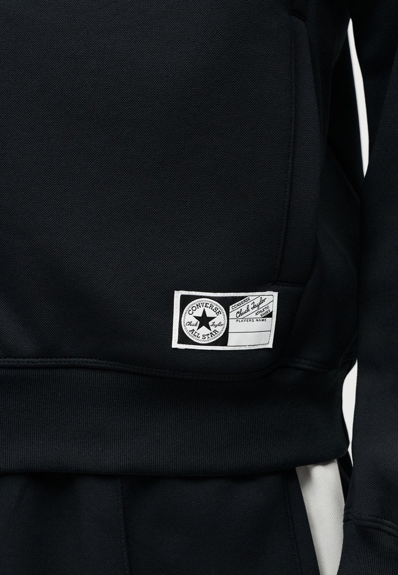 Sort sweatshirt lavet af tekstureret stof med et Converse-logo-patch, ribbet kant og sidepanelindsatser i hvid.