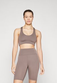 Brown sports bra and high-waisted shorts set. Made of smooth, stretchy material. Features a rounded neckline and wide straps.
