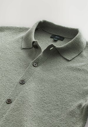 Lys grøn struktureret sweater med krave, fem brune knapper og ribbede detaljer langs kraven og knapstolpen.