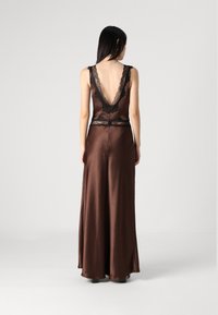 Καφέ σατινένιο φόρεμα με βαθύ V-ανοιχτή πλάτη, δαντέλα και εφαρμοστό κορσέ που ρέει σε αέρινη φούστα. Χωρίς ορατά μοτίβα ή μεταλλικά στοιχεία.