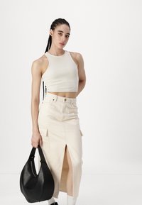 Beige ribbestrikket tank topp kombinert med et høy midje, knelange, beige denimskjørt med en frontsliss og sidelommer; holder en svart veske.