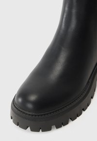 Sorte lær ankle boots med rund tå og kraftig gummisåle som har et dypt mønster. Glatt tekstur med sydd sømdetalj.