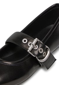 Scarpa in pelle nera con punta arrotondata, caratterizzata da una fascia larga fissata da una fibbia in metallo argentato e occhielli per la regolazione.