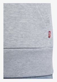 Felpa grigia realizzata in tessuto morbido, caratterizzata da un orlo a coste e un piccolo etichetta rossa Levi's sul lato. Texture liscia con un design informale.