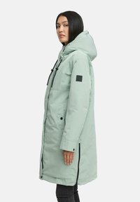 Mintgrüner langer Parka mit Kapuze, ausgestattet mit schwarzem Zubehör, einem Reißverschluss, seitlichen Taschen und verstellbaren Zugbändern. Glatte Textur.