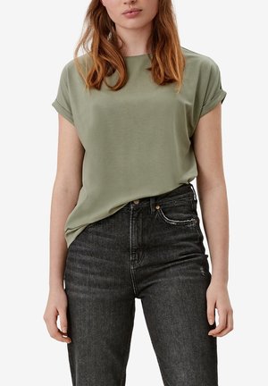 Vrouw draagt een olijfgroen kort mouw shirtje in een hoog getailleerde zwarte spijkerbroek met opgerolde pijpen.