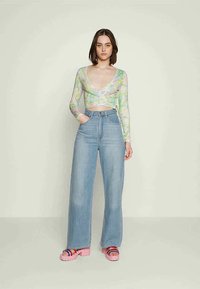 Blusa de mangas longas, transparente, com um padrão abstrato em tons pastel, combinada com jeans de perna larga de cintura alta em azul claro e sandálias de plataforma rosas.