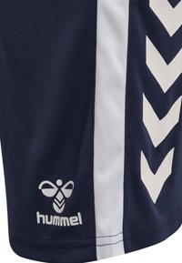 Marinblå shorts med vita sidestreck och ett chevronmönster. Inkluderar en liten logotyp med texten "hummel" i vitt längst ner. Mjuk tygtextur.