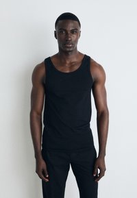 Sort ærmeløs tanktop lavet af glat stof, tætsiddende design med rund halsudskæring, parret med matchende sorte bukser, minimalistisk look.