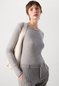 Grå ribbet langermet topp med rund hals, sammen med bukser i sypelsmønster i grått. En ensfarget lyse bag bæres over den ene skulderen.
