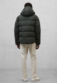 Mørkegrøn polstret jakke med hætte, med et quiltet design, båret sammen med lyse beige bukser og hvide sneakers.