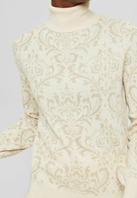 Krämfärgad polokragetröja med subtilt beige utsmyckad blomster-damaskmönster, långa ärmar och ribbade ärmslut.