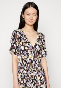 Vestido floral em castanho escuro, com um decote em V profundo, mangas curtas e uma cintura amarrada. Os padrões incluem flores lavanda, creme e maroon.