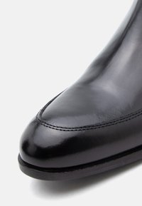 Pantof negru din piele cu un design elegant, vârf rotunjit și cusături subtile de-a lungul părții superioare. Finisaj neted, lucios, cu toc mic.