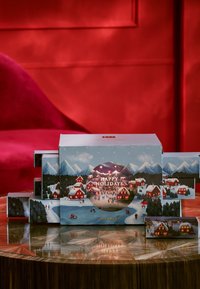 Urlaubs-Geschenkbox mit einer Illustration eines verschneiten Dorfes, blauen und weißen Farbschema, ausgestattet mit Schubladen zum Herausziehen und einem kreisförmigen "Frohe Feiertage"-Design.