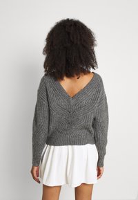 Grå stickad tröja med V-ringning, prydd med ett texturerat mönster och sänkt axel, matchad med en vit lagerkjol.