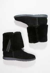 Stivaletti in camoscio nero con collo in pelliccia e suola in gomma grigia. Dettaglio logo laterale e cuciture a contrasto. Esterno flessibile e strutturato.