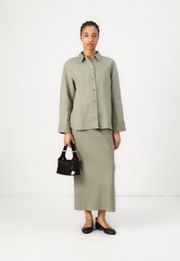 Olive-green linen shirt with buttons, matching fitted skirt, and black small handbag. Black flats complete the outfit. Smooth, minimal texture.