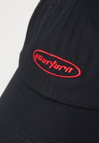 Svart cap laget av bomull med en strukturert krone, med et rødt brodert logo i oval form foran. Klassisk buet skjerm.