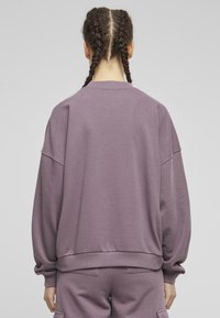Oversized lila sweatshirt med sänkt axel, ribbade muddar och fåll. Slät textur, avslappnad design och ledig passform.